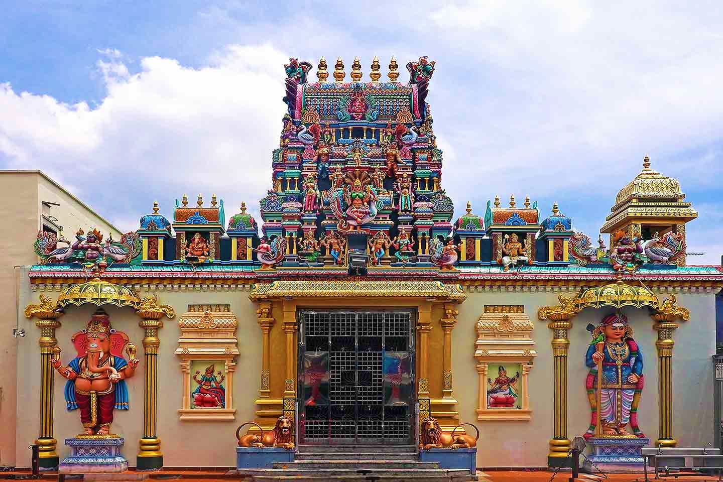 Colorful Hindu temple facade with ornate golden gopuram tower, detailed deity sculptures, and traditional architectural eleme